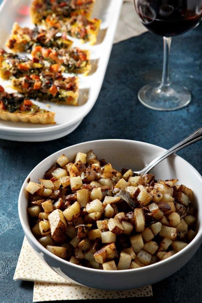 home fries and quiche on a blue table with wine