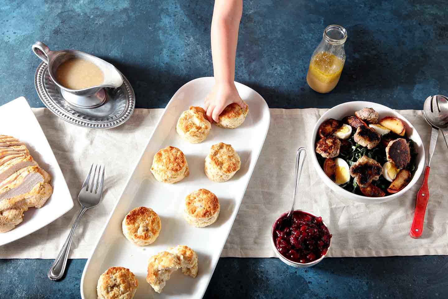 A girl grabs for a Thanksgiving Turkey Biscuit on a blue table