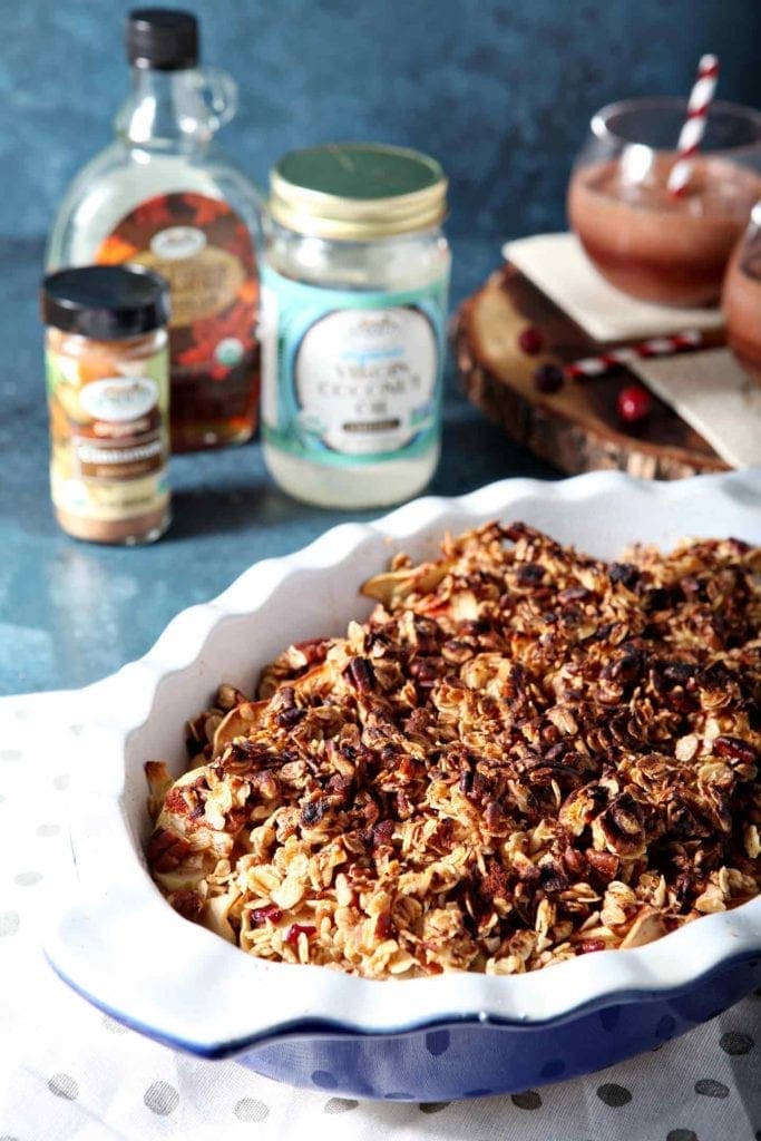 Close up of the Vegan Apple Crisp in a blue baking dish with the ingredients in jars behind it