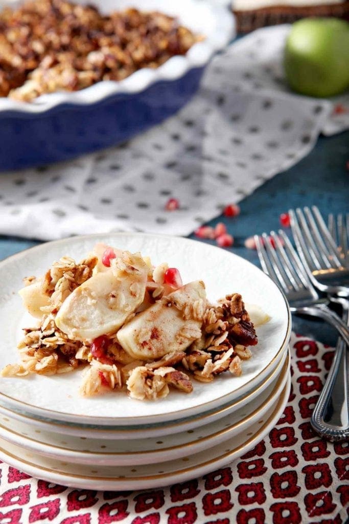 Close up of a serving of apple crisp with pomegranates on a stack of white plates