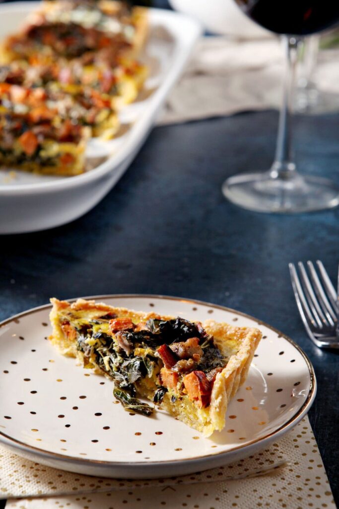 A slice of sweet potato quiche with collards and sausage on a plate