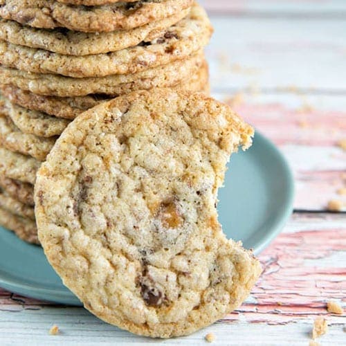 A vertical stack of toffee crunch cookies with one in front with a bite in it on a wooden countertop.