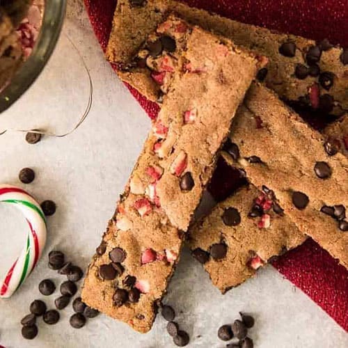Stack of peppermint chocolate chip cookie sticks spilling over a red christmas plate onto parchment paper