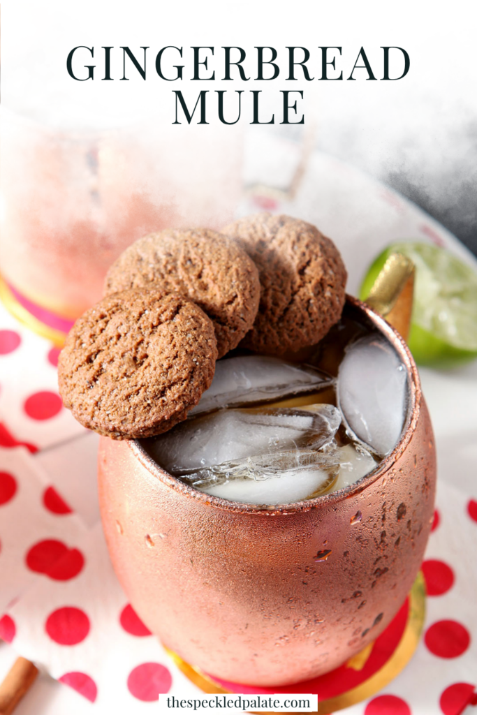 Two copper mugs of drinks, garnished with three gingersnaps on the rim, sit on a white tray with decorative red and white napkins with the text gingerbread mule