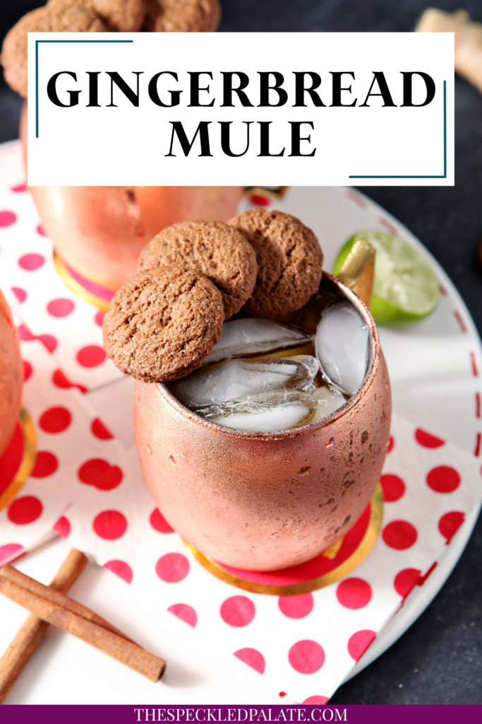 Two copper mugs of drinks, garnished with three gingersnaps on the rim, sit on a white tray with decorative red and white napkins with the text gingerbread mule