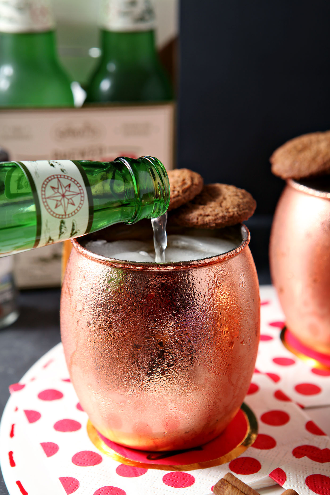 Ginger beer pours into a copper mug on a white platter in front of a container of ginger beer