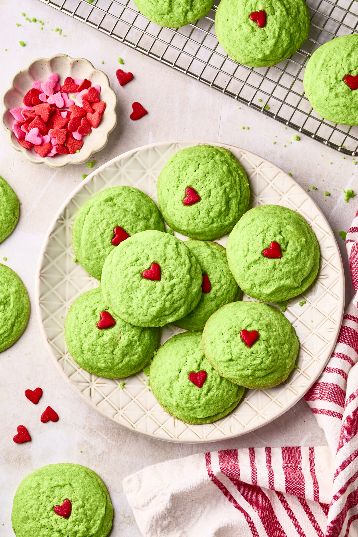 A plate of green Grinch cookies with red hearts in the center of each cookie.