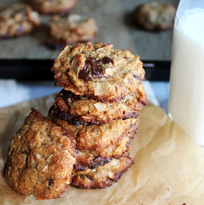 A stack of coconut chocolate chip cookies on brown parchment paper with a glass of milk.