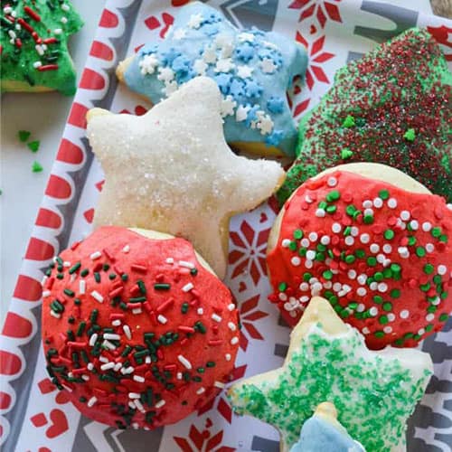 Lofthouse Cut Out Christmas cookies on a plate alternating star shaped cookies and circle shape. Decorated in various christmas frosting adn with various sprinkles.