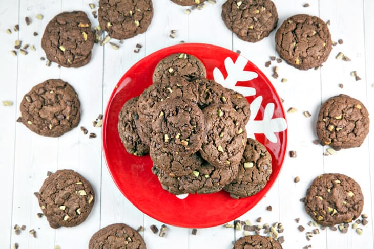A red christmas plate filled with chewy chocolate mint cookies and surrounded by gold glitter and ten cookies around the plate