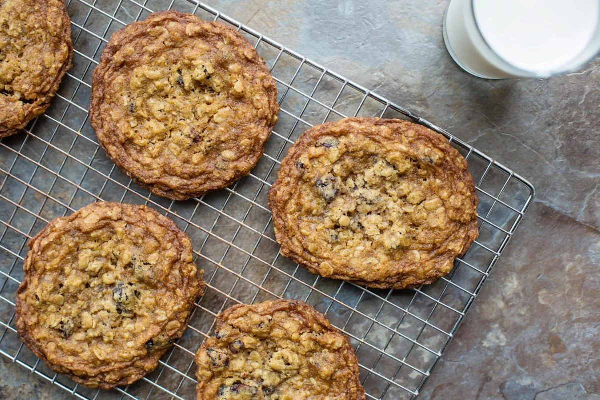 A drying rack with five Oatmeal Cookies on it and a glass of milk off to the right side.