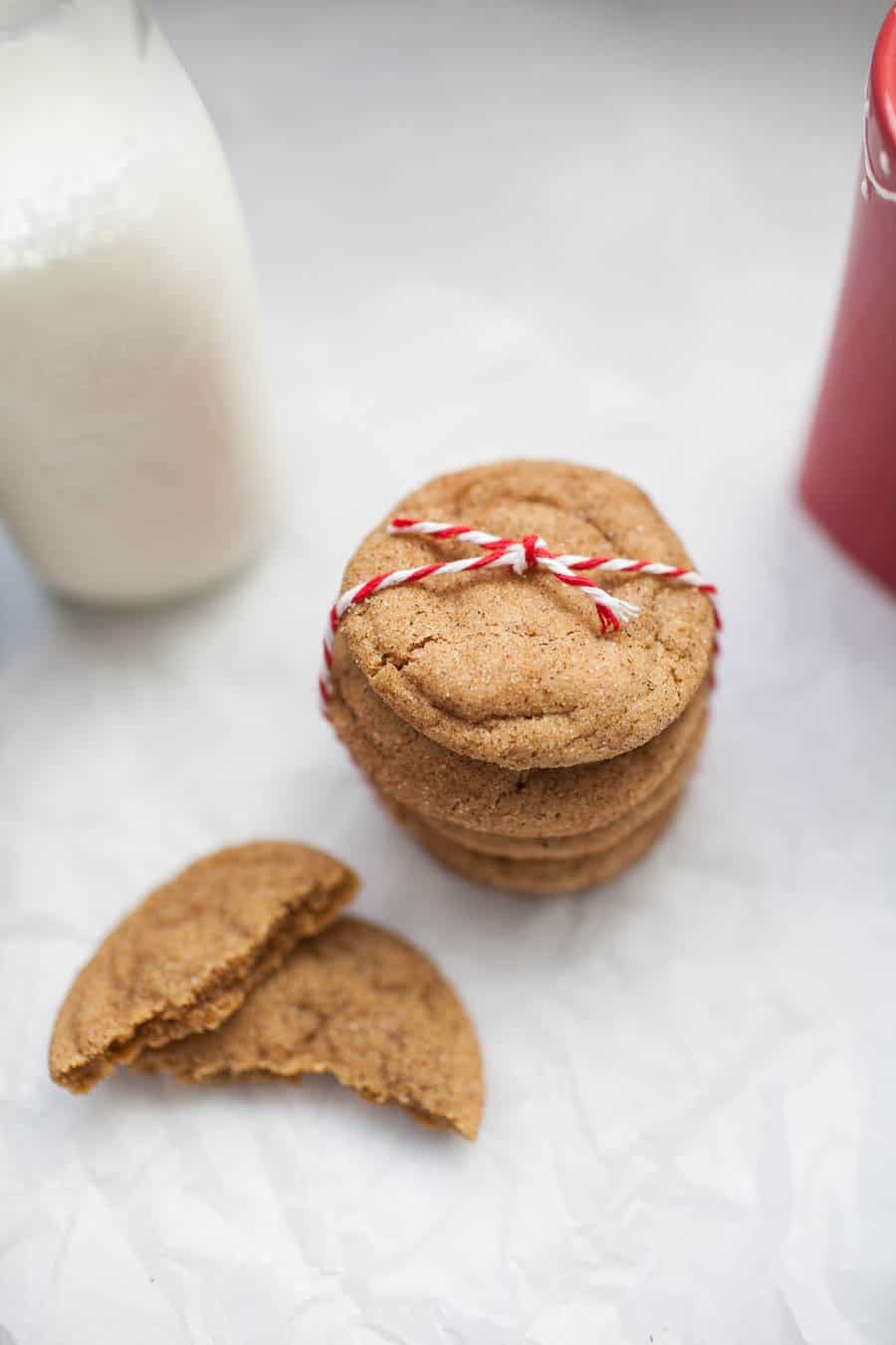 An overhead view of a stack of ginger molasses snickerdoodle cookies warpped with a red and white string along with a glass of milk and half eaten cookie.
