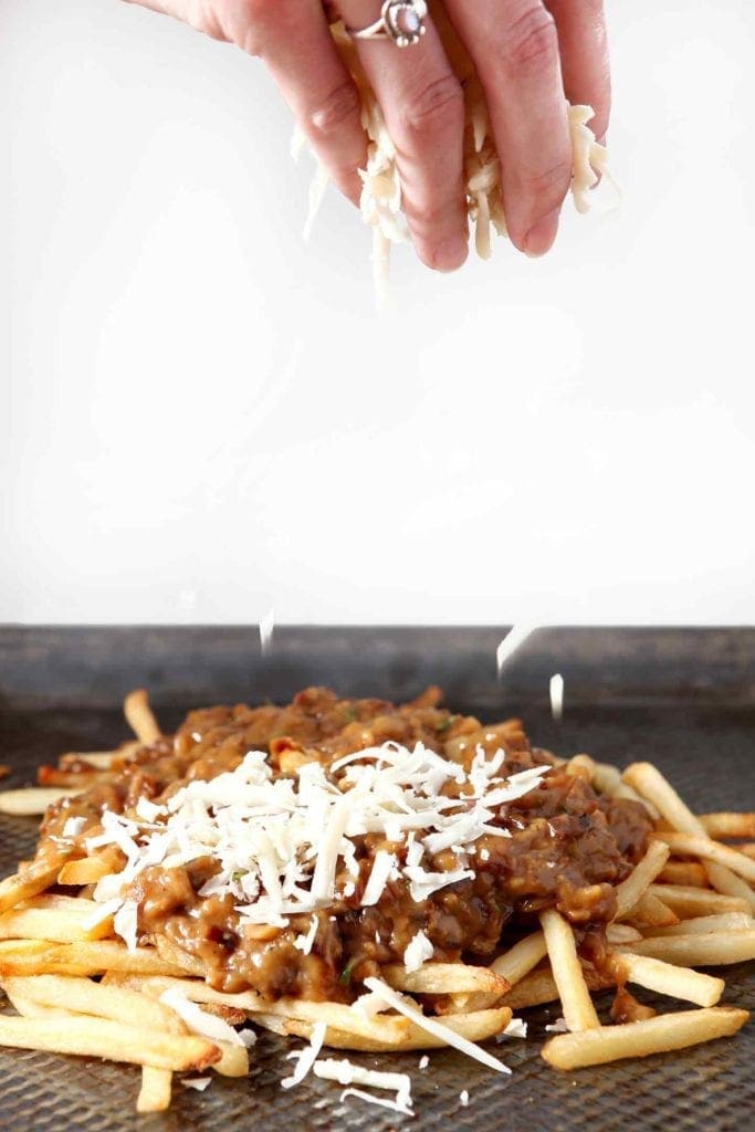 sprinkling cheese over french onion poutine