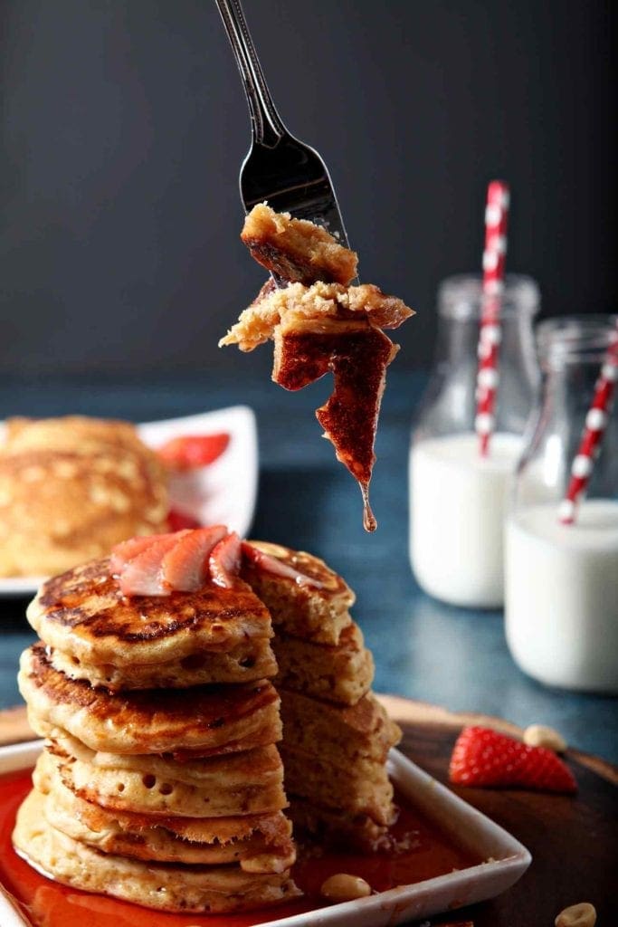 bite of pancakes on a fork, milk in the background