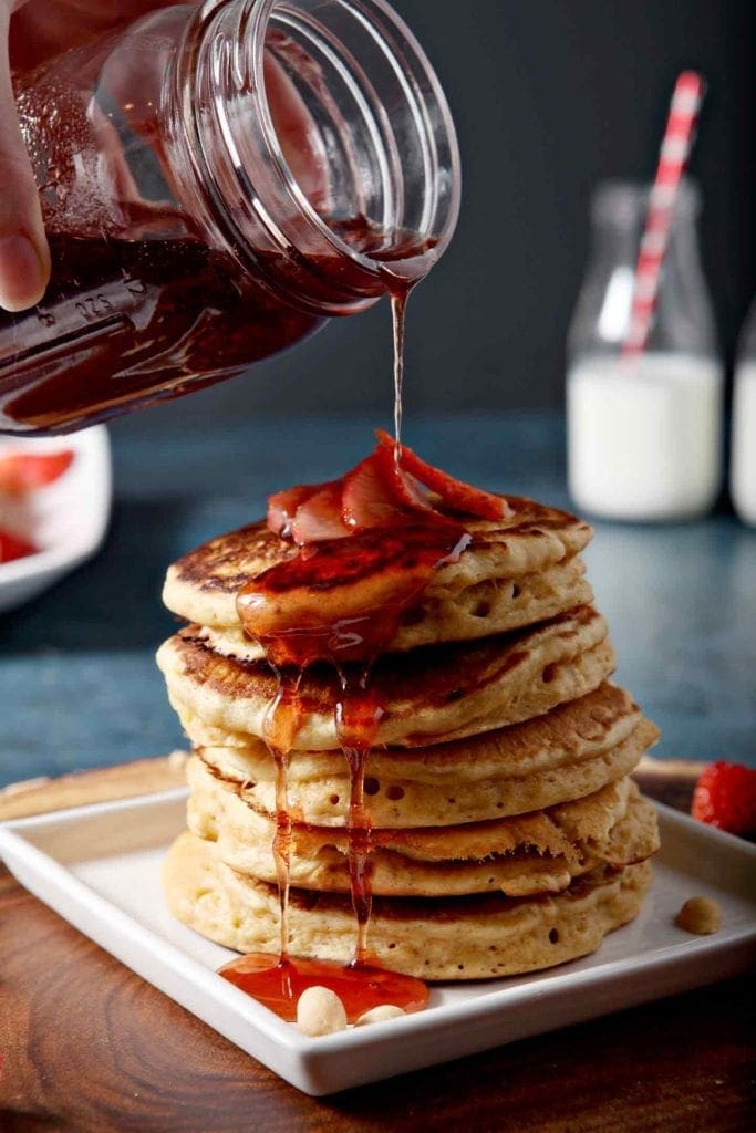 pouring syrup on a stack of pancakes