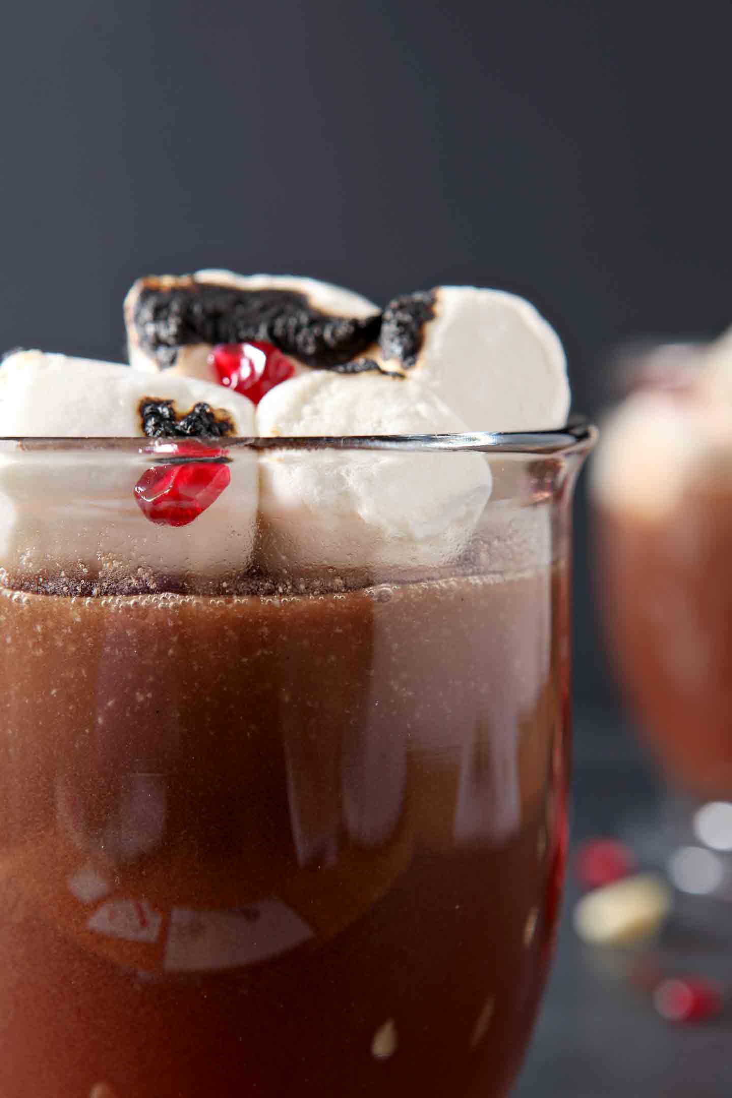 close up of pomegranate white hot chocolate in a glass with marshmallows