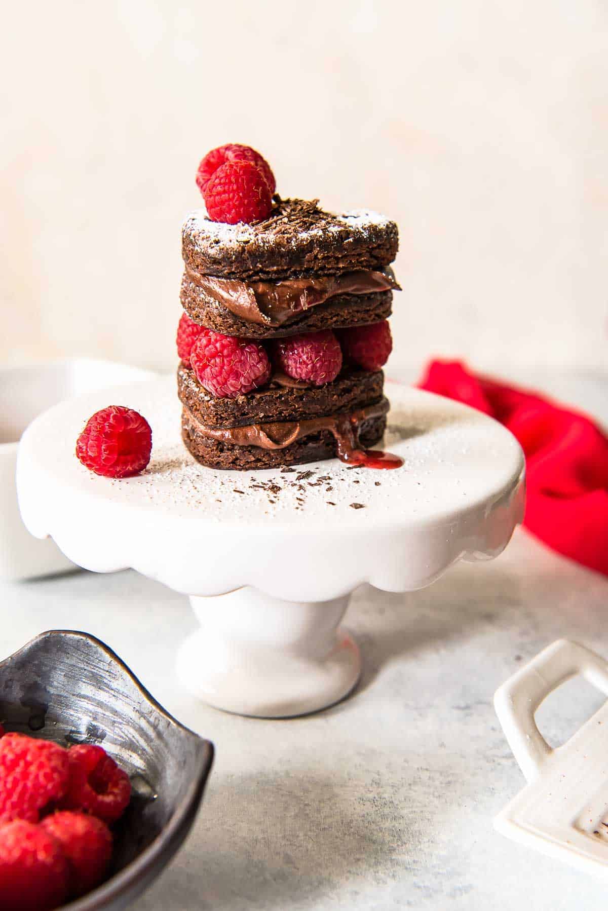 Mini Brownie Layer Cakes with Raspberry Coulis stacked on a tiny cake stand and decorated with fresh raspberries