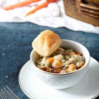 chicken pot pie in a white bowl with a biscuit