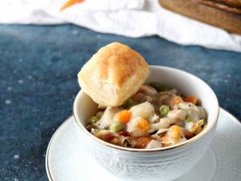 chicken pot pie in a white bowl with a biscuit