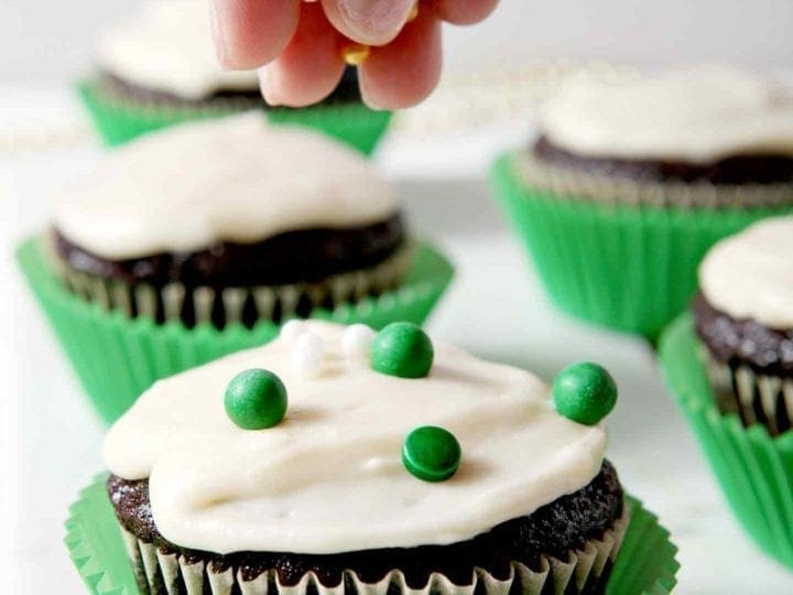 Chocolate Guinness Cupcakes, iced with Bailey's Icing, being decorated with green, white and gold sprinkles