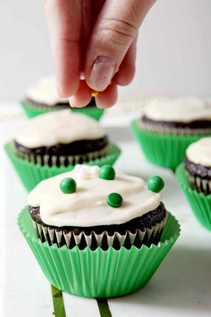 Irish Car Bomb Cupcakes, iced with Baileys Frosting, are decorated with green, white and gold sprinkles