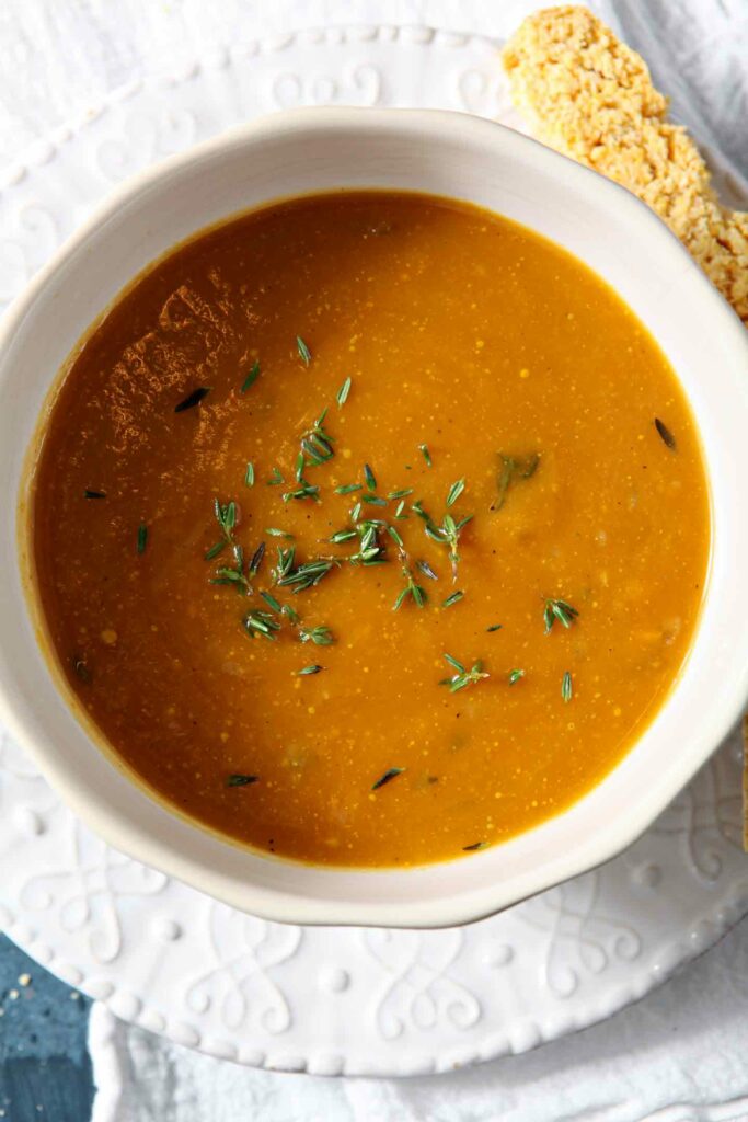 Two bowls of Sweet Potato Bisque on a blue background with cornbread biscotti