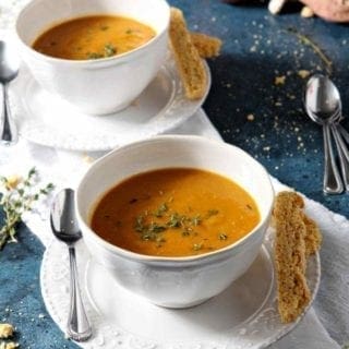 Two bowls of Sweet Potato Bisque on a blue background with cornbread biscotti