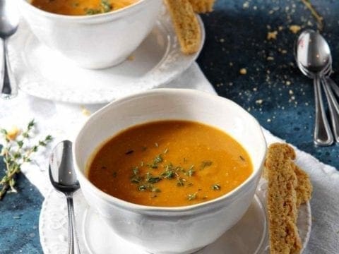 Two bowls of Sweet Potato Bisque on a blue background with cornbread biscotti