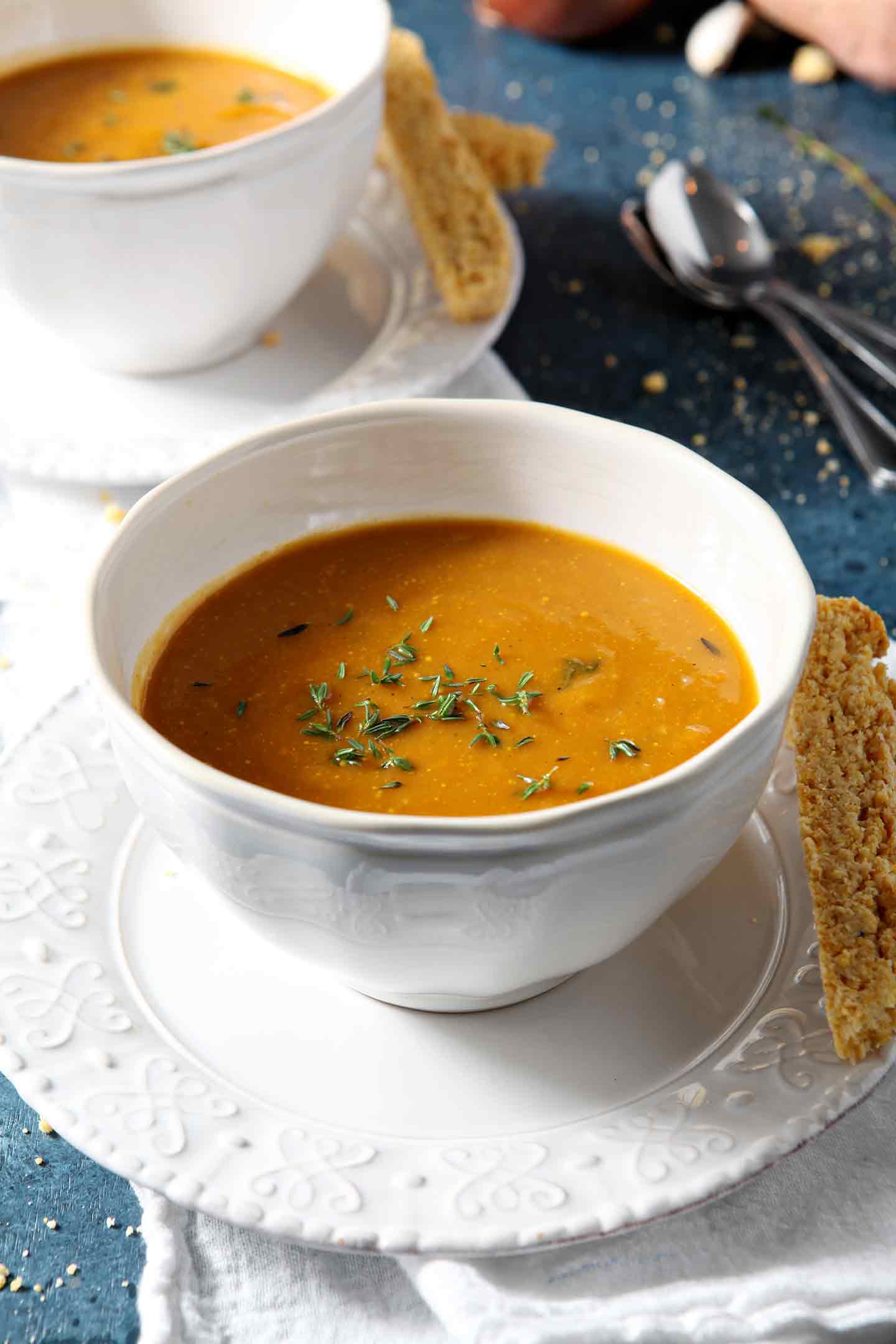 Savory, smooth and flavorful, Sweet Potato Bisque is chock full of sweet potato goodness. | Sweet Potato Bisque | Sweet Potato Soup | Vegetarian Sweet Potato Soup | Vegetarian Soup | Whole30 Soup | Whole30 Sweet Potato Soup | Paleo Sweet Potato Soup | Paleo Soup | Sweet Potato Entree | Winter Soup | Comfort Food | Curried Sweet Potato Soup Two bowls of Sweet Potato Bisque on a blue background with cornbread biscotti