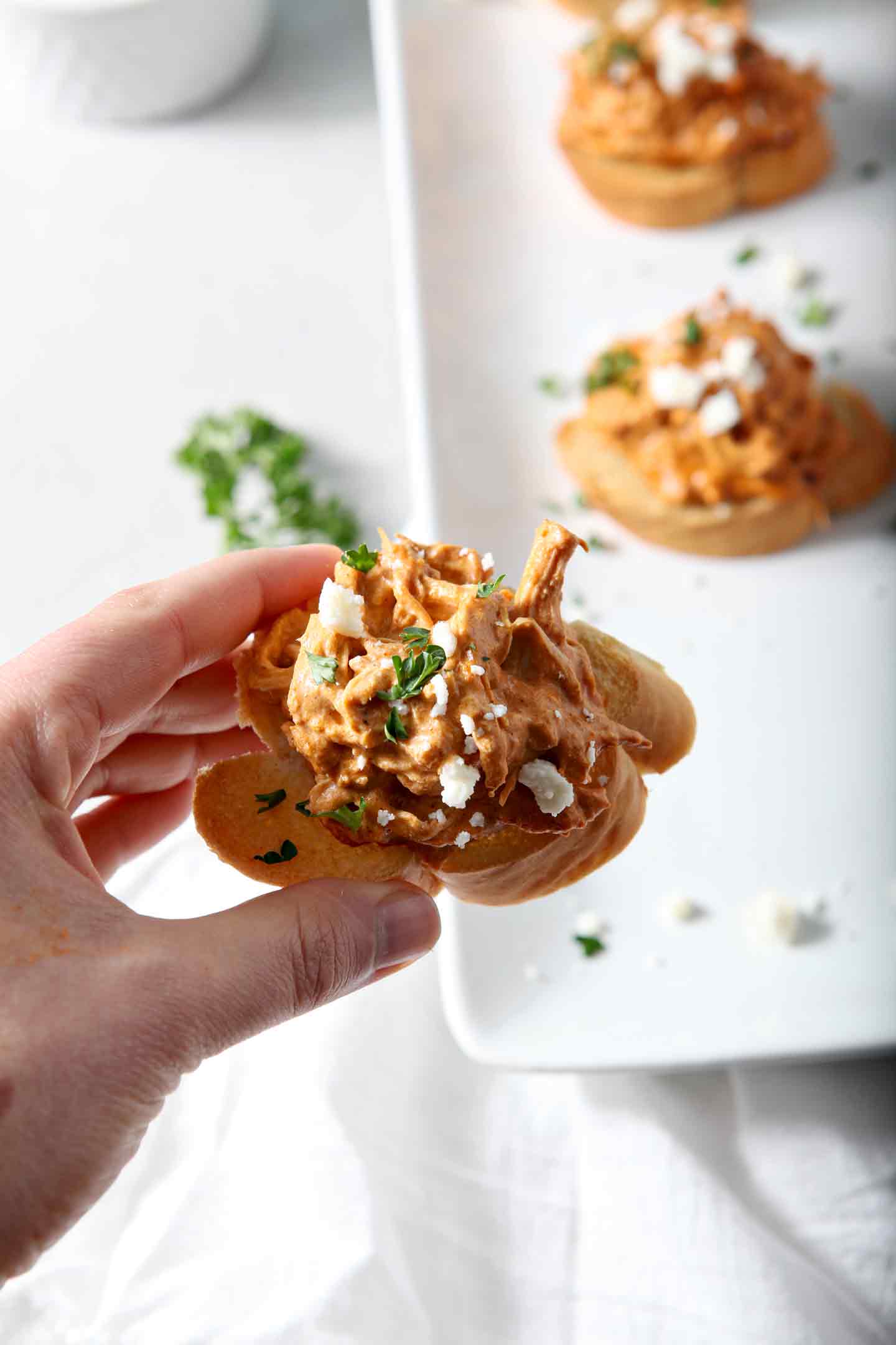 A hand holding Chicken Enchilada Bruschetta over a platter of the appetizer before eating