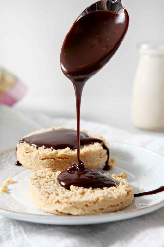 One Irish Cream Biscuit cut in half, being drizzled with Baileys Chocolate Ganache