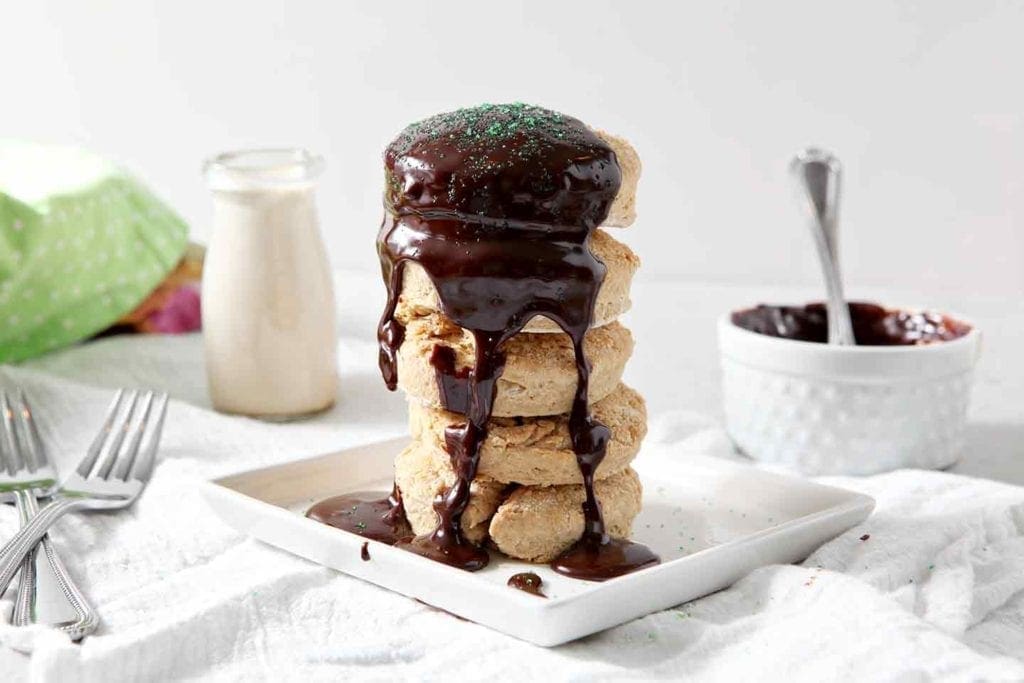 Irish Cream Biscuits stacked on top of each other and drizzled with Boozy Chocolate Ganache on a white background with other biscuits in the background