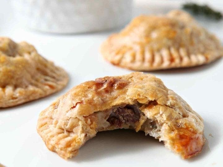 Closeup of a bitten-into Mashed Potato Beef Hand Pies with others on a white platter
