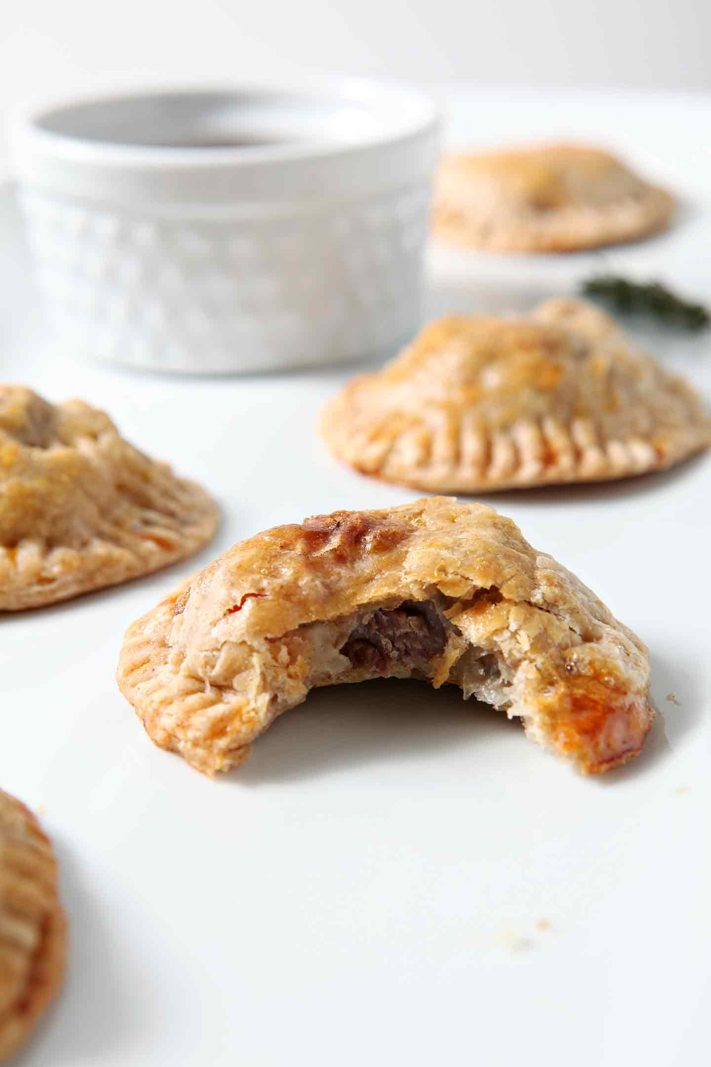 Closeup of a bitten-into Mashed Potato Beef Hand Pies with others on a white platter