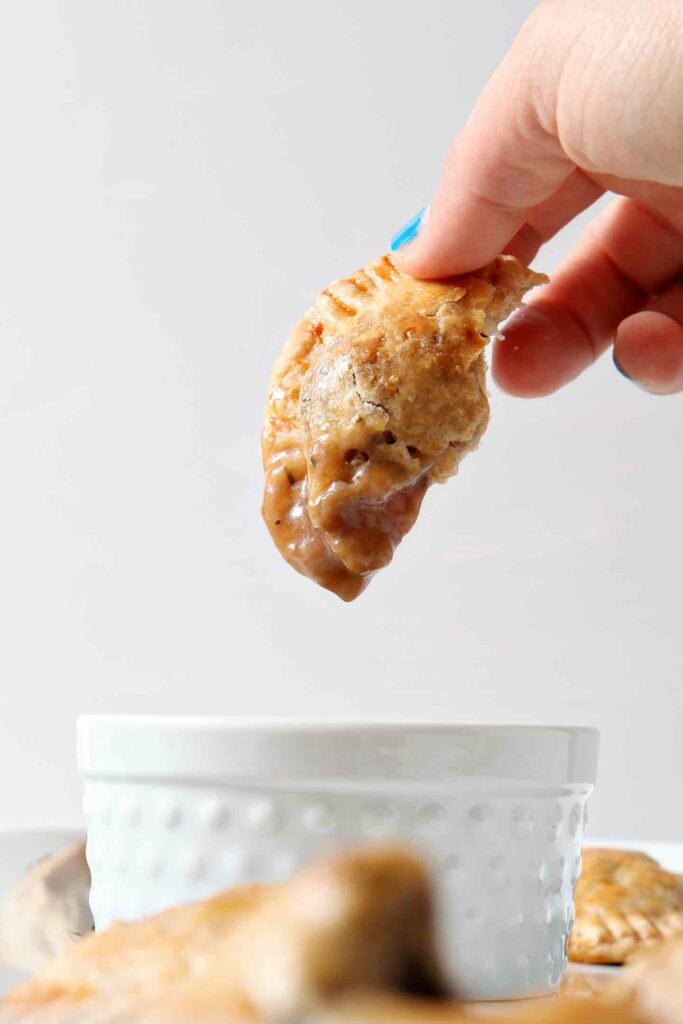 A woman dips a Irish meat pie into a white container holding gravy