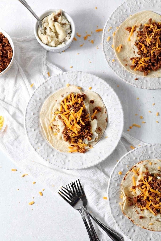 Three white plates holding prepared Mashed Potato Chorizo Breakfast Tacos from above