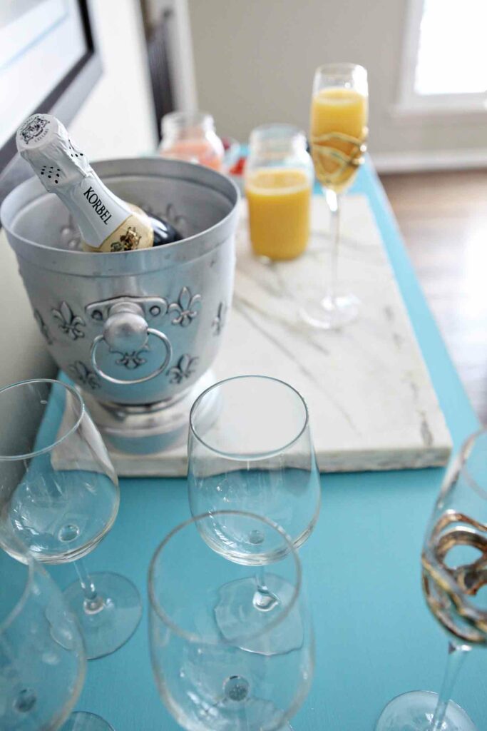 A bar is set up on a turquoise piece of furniture, complete with glassware on display, champagne in an ice bucket and more