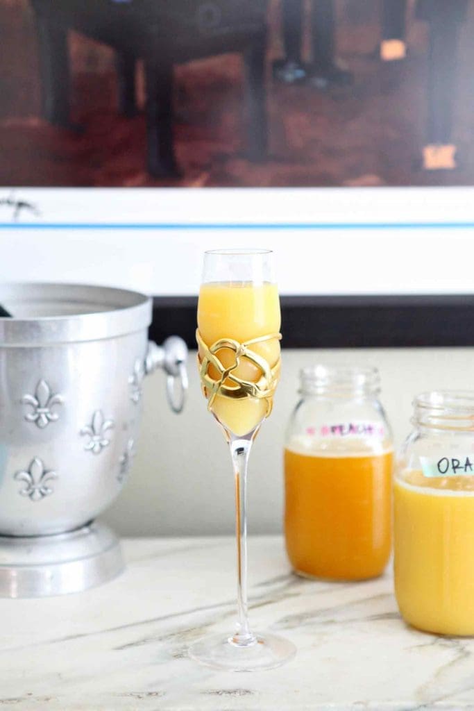 A bellini (a champagne and peach juice cocktail) sits on a marble slab, surrounded by jars holding other juices and champagne