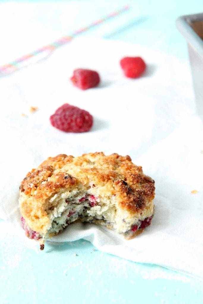 One half-eaten Raspberry Shortcake Biscuit sits on a white flour sack with raspberries scattered behind it