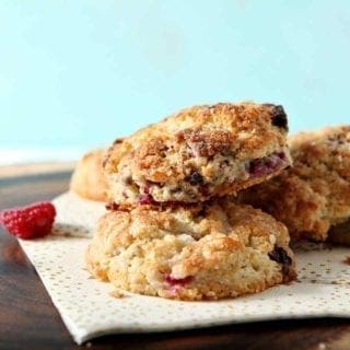 A pile of Raspberry Shortcake Biscuits sit on a wooden platter while surrounded with raspberries