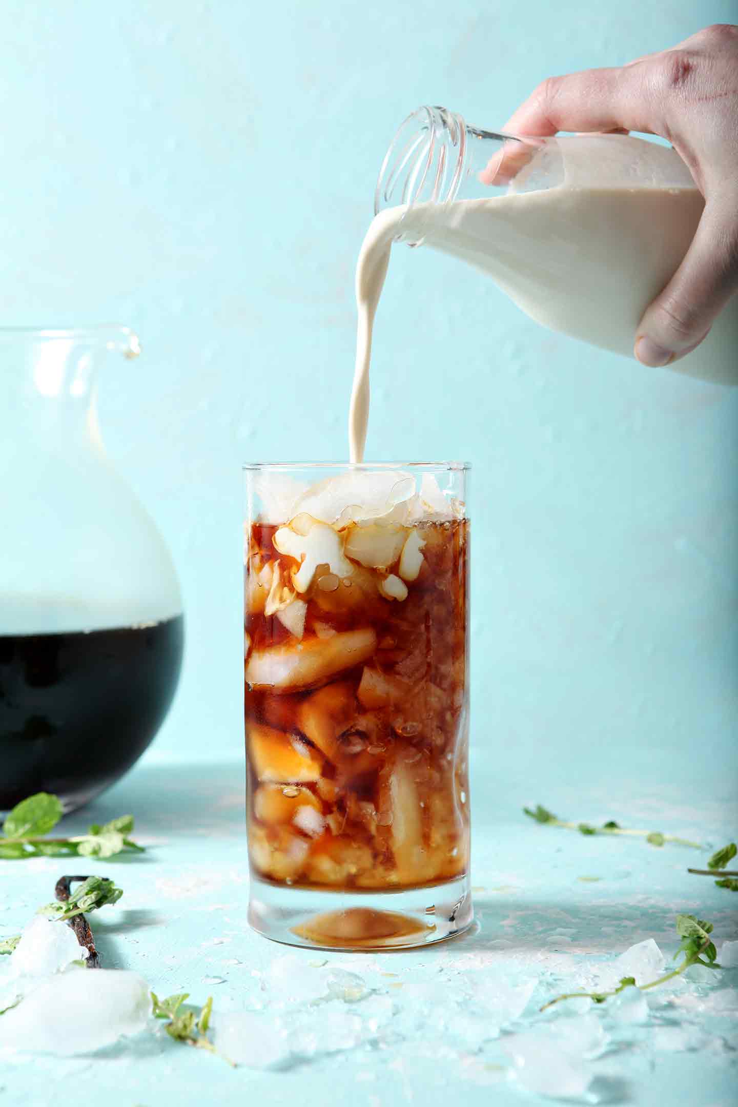 Homemade Vanilla Mint Creamer is poured over Dunkin' Donuts Cold Brew in a tall glass on a turquoise background