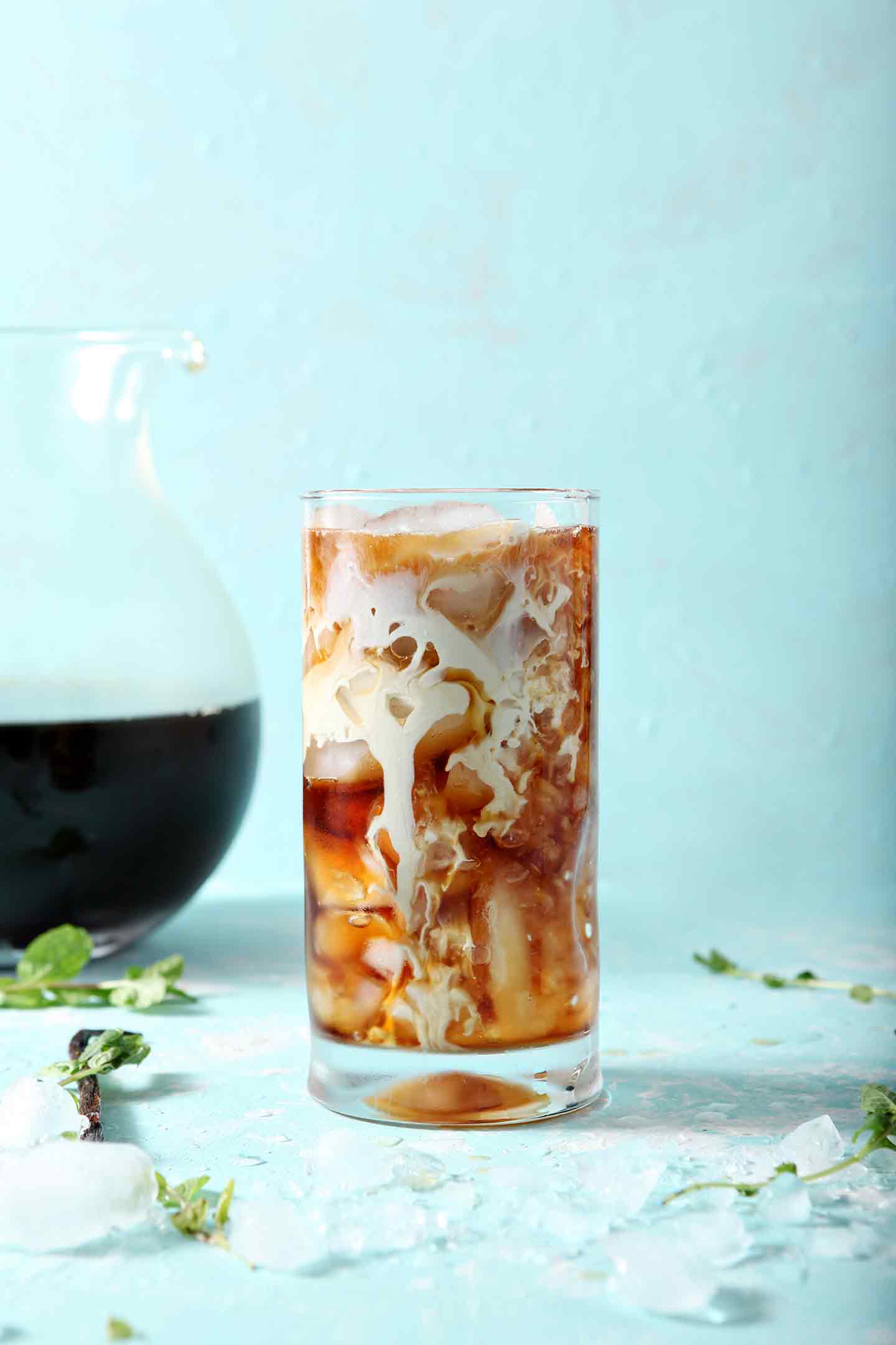 Homemade Vanilla Mint Creamer swirling into a glass of Dunkin' Donuts Cold Brew on a turquoise background