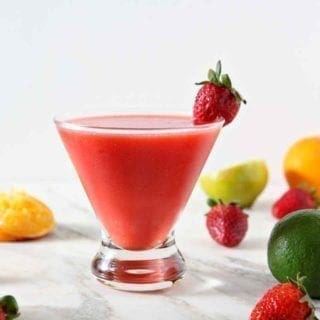 A Strawberry Virgin Margarita sits on a marble background, surrounded by strawberries, limes and oranges.