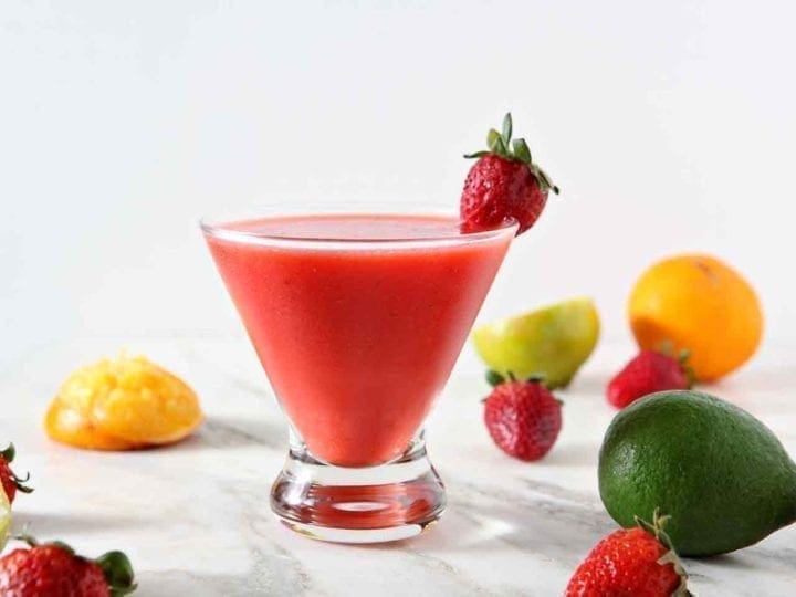 A Strawberry Virgin Margarita sits on a marble background, surrounded by strawberries, limes and oranges.
