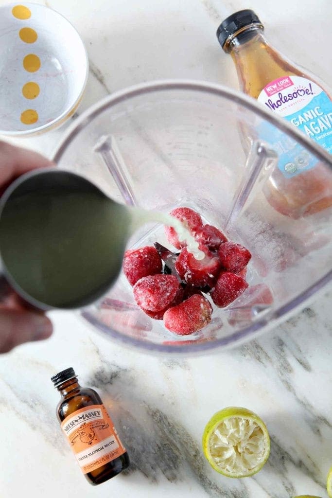 Lime juice is poured into a blender with frozen strawberries before a Strawberry Virgin Margarita is made