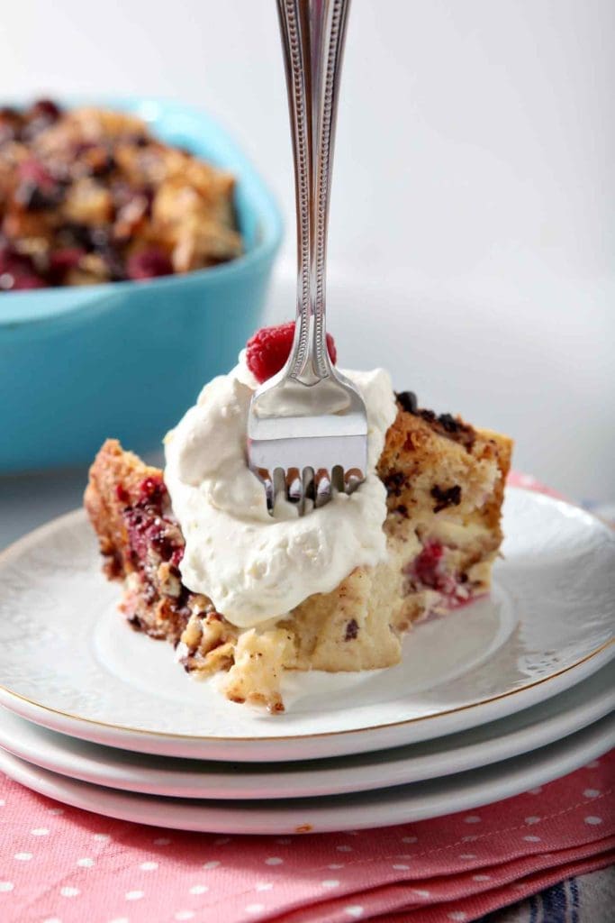 A fork cuts into a serving of Chocolate Raspberry Overnight French Toast Casserole, topped with Lemon Whipped Cream and a raspberry.