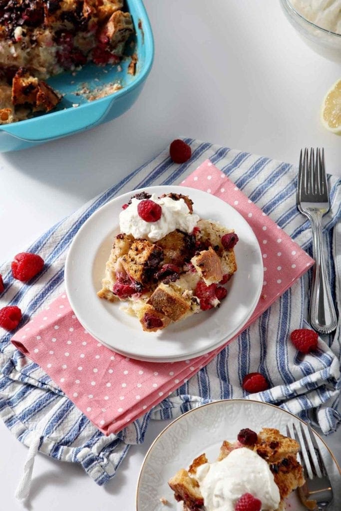 A plate of food French toast casserole with whipped cream and raspberries