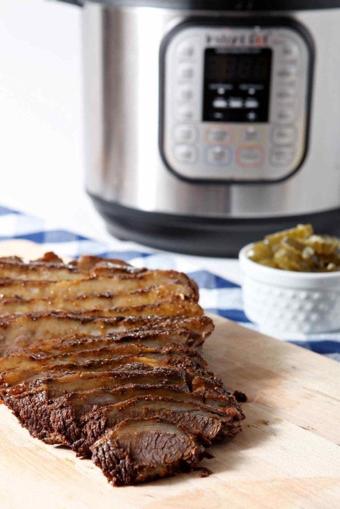 Instant Pot BBQ Brisket sits on a wooden cutting board in front of an Instant Pot after cooking and slicing.