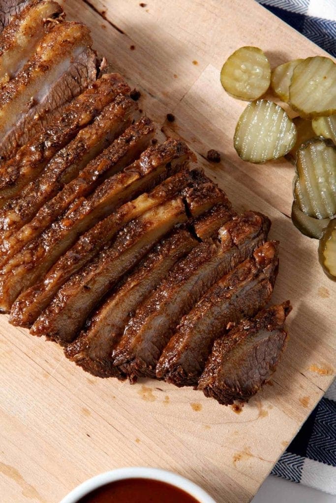 Overhead image of Instant Pot BBQ Brisket, shown on a wooden cutting board, served with barbecue sauce and pickles