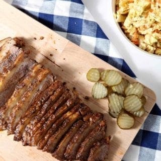 Overhead image of Instant Pot BBQ Brisket, served on a wooden platter with pickles, and other barbecue sides.